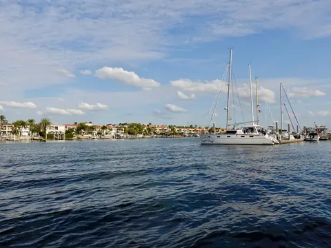 Sailboats moored on blue water before a row of waterfront homes and palms