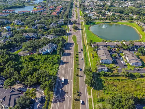 An aerial view of a green Florida suburb with homes, a pond and a divided road
