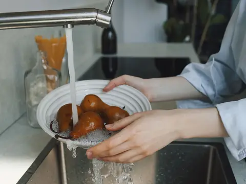 Hands washing pears under a kitchen faucet