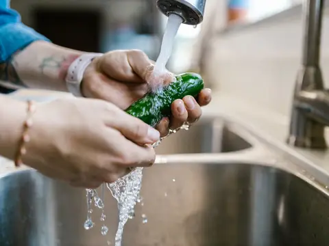 Hands rinsing a cucumber under a running kitchen faucet