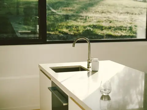 A kitchen sink and faucet at a wide window, a glass of water on the white counter
