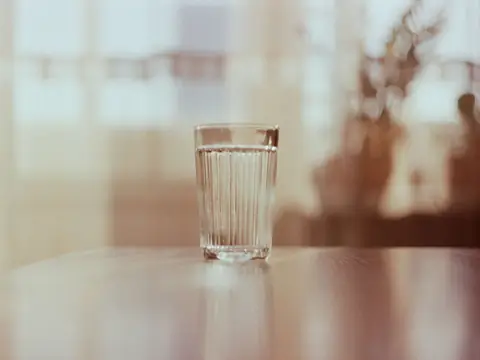 A glass of water on a table against a bright, sunny background