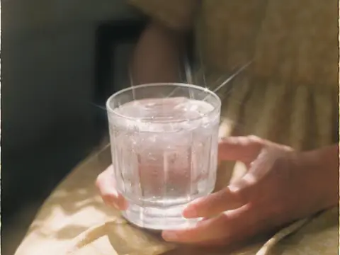 Hands holding a glass of water sparkling in soft sunlight