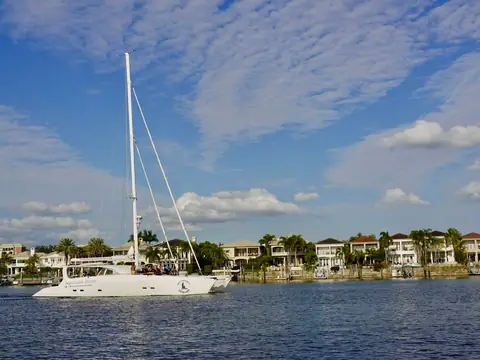 A sailing yacht passing waterfront homes under a blue sky