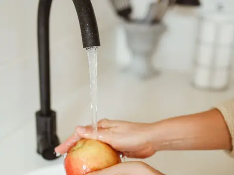 Hands rinsing an apple under a black kitchen faucet
