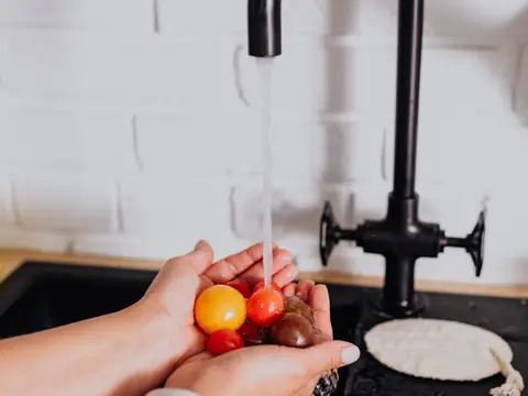 Hands rinsing cherry tomatoes under a black kitchen faucet