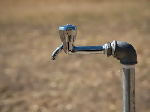 A metal water tap on a pipe standing in an open field