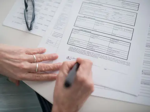A hand signing a printed form with a pen