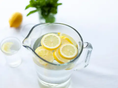 A glass pitcher of water with lemon slices on a white table