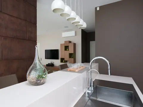 A chrome faucet over a steel sink at a white kitchen counter with a glass vase