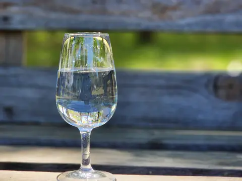 A clear glass of water on a wooden bench outdoors in sunlight