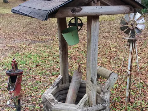 A wooden well with a shingled roof and a hand pump in a yard in Morriston, Florida