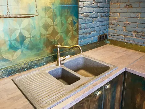 A double stone kitchen sink with a brass faucet against a blue brick wall